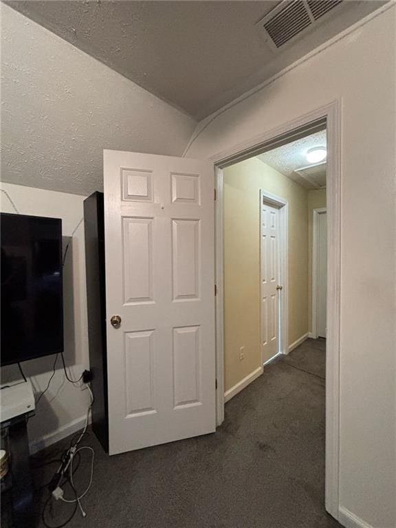 hall with baseboards, visible vents, dark colored carpet, and a textured ceiling