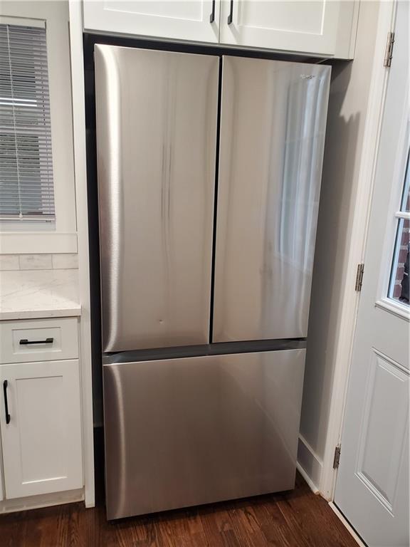 room details with dark wood-type flooring, light stone countertops, stainless steel refrigerator, and white cabinets