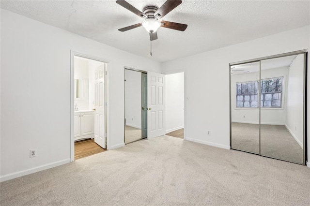 unfurnished bedroom with connected bathroom, light carpet, a textured ceiling, multiple closets, and ceiling fan