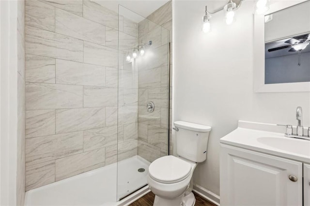 bathroom with a tile shower, wood-type flooring, vanity, ceiling fan, and toilet