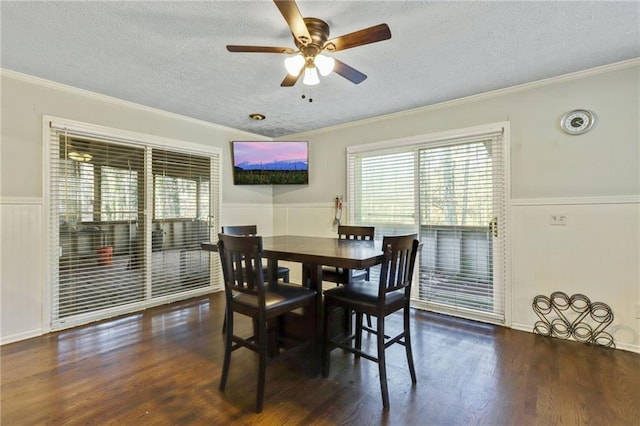 dining space with a textured ceiling, a wainscoted wall, a ceiling fan, dark wood finished floors, and crown molding