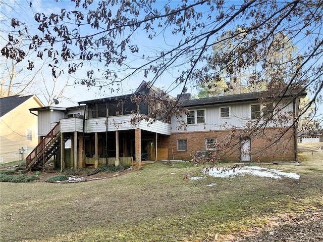 back of house featuring brick siding, a sunroom, stairs, a lawn, and a chimney