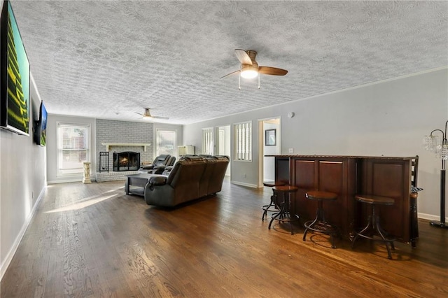 living area featuring ceiling fan, a fireplace, baseboards, dark wood-style floors, and a bar