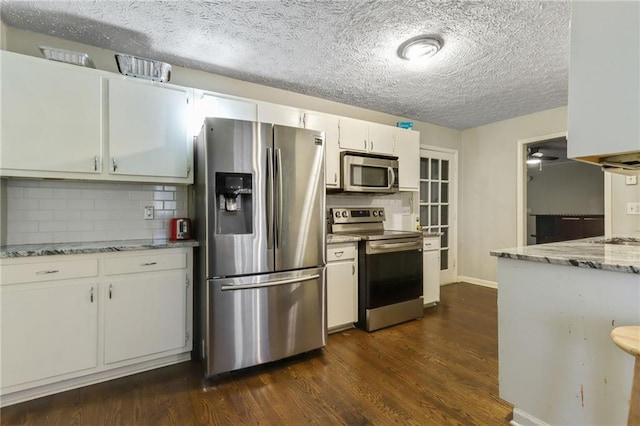 kitchen featuring white cabinets, appliances with stainless steel finishes, backsplash, light stone countertops, and dark wood-style floors