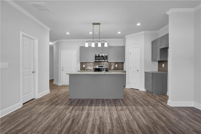 kitchen with hanging light fixtures, a center island with sink, appliances with stainless steel finishes, gray cabinets, and backsplash