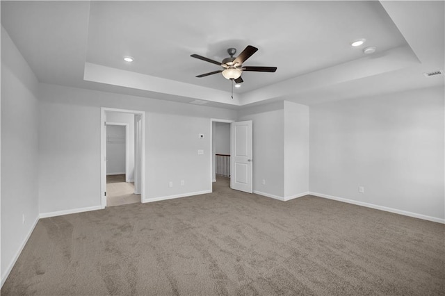 unfurnished bedroom with a spacious closet, a raised ceiling, ceiling fan, and carpet