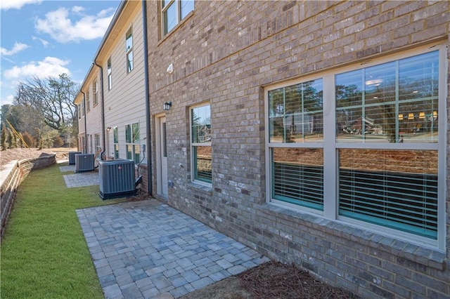 view of side of home with central AC unit, a yard, and a patio