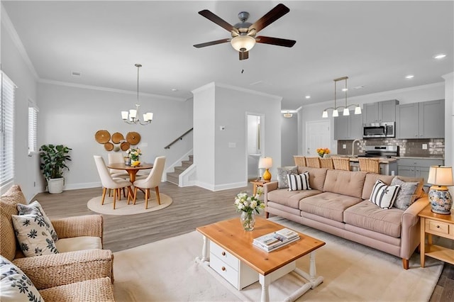 living room with crown molding, ceiling fan with notable chandelier, sink, and light wood-type flooring