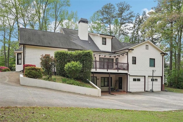 back of property with concrete driveway, a deck, a garage, and a chimney