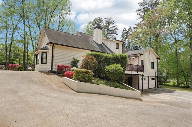 view of side of property with a chimney, a garage, a wooden deck, and aphalt driveway