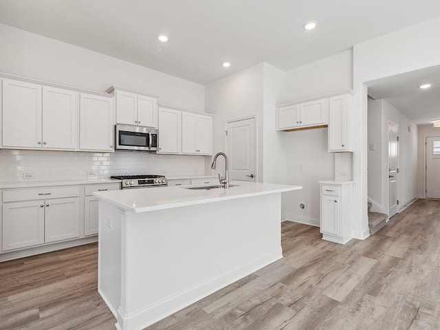 kitchen featuring an island with sink, light wood-style flooring, a sink, stainless steel microwave, and backsplash