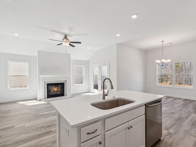 kitchen featuring a premium fireplace, a kitchen island with sink, a sink, stainless steel dishwasher, and open floor plan