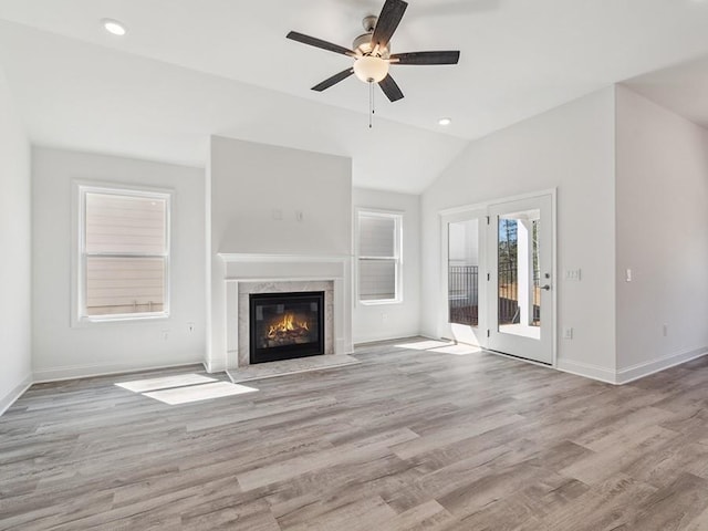 unfurnished living room featuring baseboards, light wood-type flooring, a premium fireplace, vaulted ceiling, and a ceiling fan