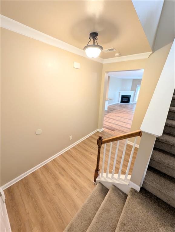 staircase featuring wood finished floors, crown molding, baseboards, and a fireplace