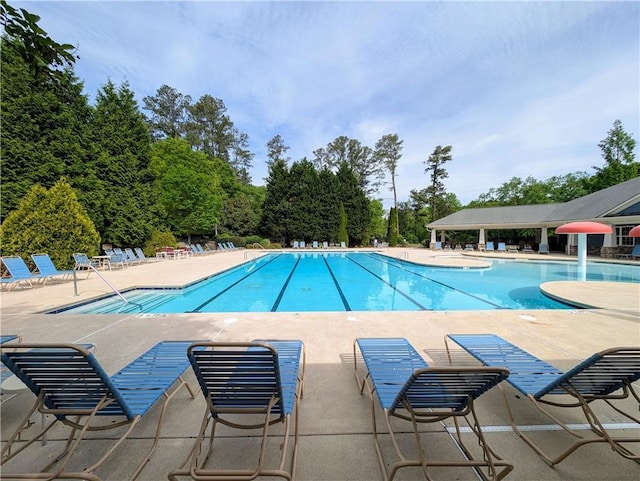 community pool with a patio and view of wooded area