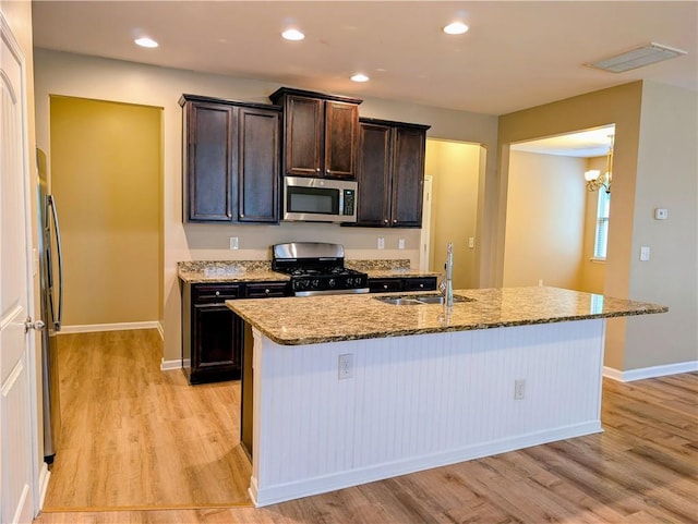 kitchen with appliances with stainless steel finishes, a sink, light wood finished floors, light stone countertops, and recessed lighting