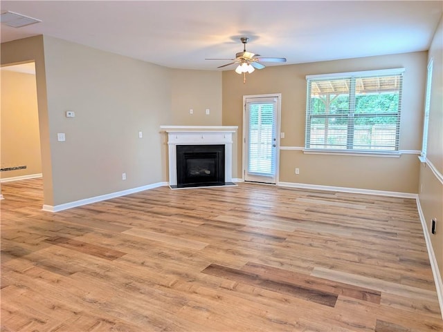 unfurnished living room with a ceiling fan, light wood finished floors, a glass covered fireplace, and baseboards