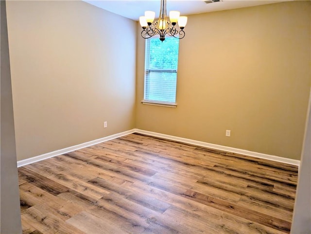 spare room featuring a chandelier, wood finished floors, and baseboards