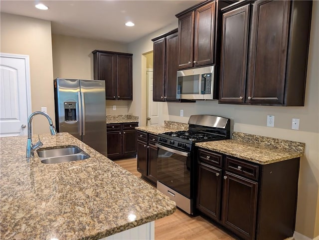 kitchen featuring stainless steel appliances, a sink, light wood-style floors, dark brown cabinetry, and light stone countertops
