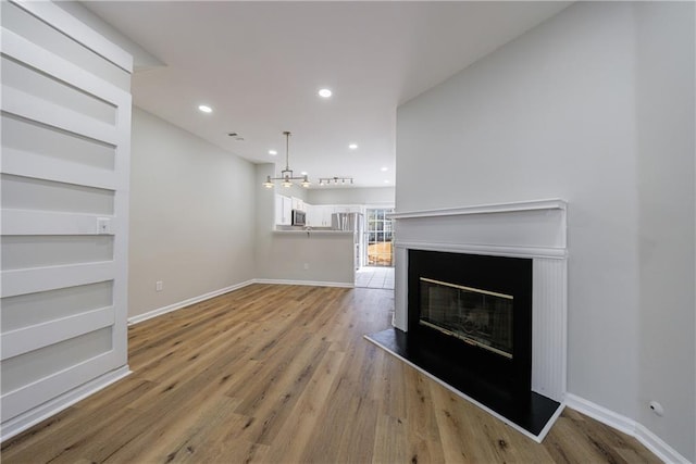 unfurnished living room featuring light wood-style floors, a glass covered fireplace, baseboards, and recessed lighting