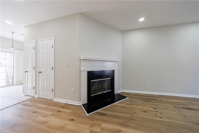 unfurnished living room featuring a premium fireplace, recessed lighting, wood finished floors, and baseboards