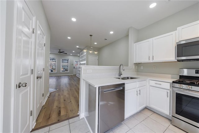 kitchen featuring appliances with stainless steel finishes, open floor plan, a peninsula, white cabinetry, and a sink