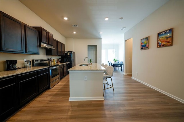 458 Bishop Ln, Woodstock, GA 30188 - kitchen featuring stainless steel range with electric cooktop, under cabinet range hood, a sink, a breakfast bar, and a center island with sink