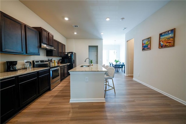 458 Bishop Ln, Woodstock, GA 30188 - kitchen featuring stainless steel electric stove, under cabinet range hood, a sink, a breakfast bar, and a kitchen island with sink