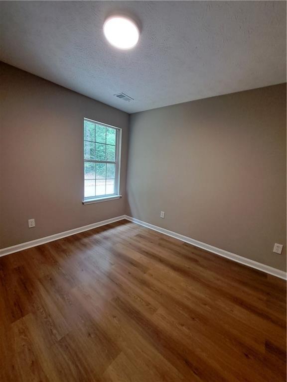 empty room with baseboards, a textured ceiling, wood finished floors, and visible vents