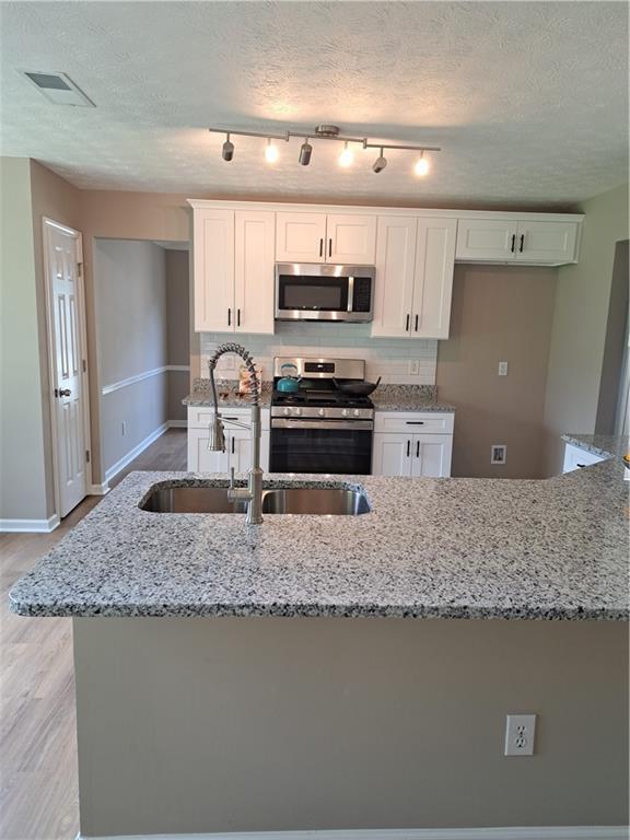 kitchen featuring light stone countertops, a sink, white cabinets, light wood-style floors, and stainless steel appliances