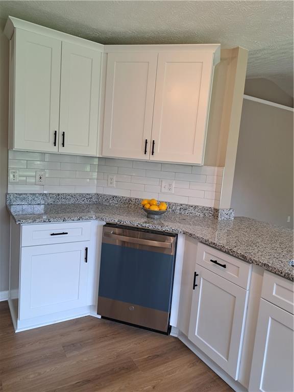 kitchen with wood finished floors, light stone countertops, dishwashing machine, white cabinets, and backsplash