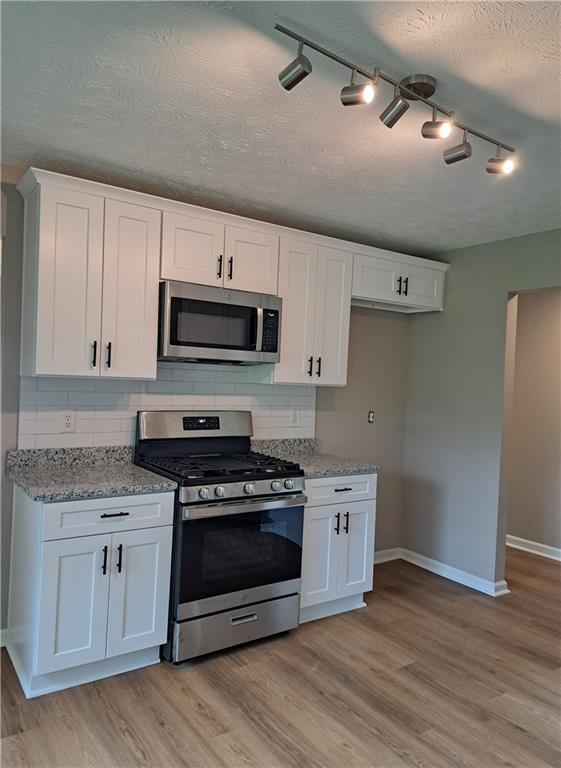 kitchen with decorative backsplash, baseboards, white cabinets, light wood finished floors, and stainless steel appliances