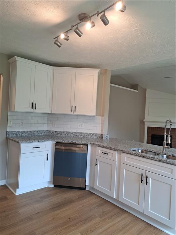 kitchen with a sink, dishwashing machine, white cabinets, and tasteful backsplash