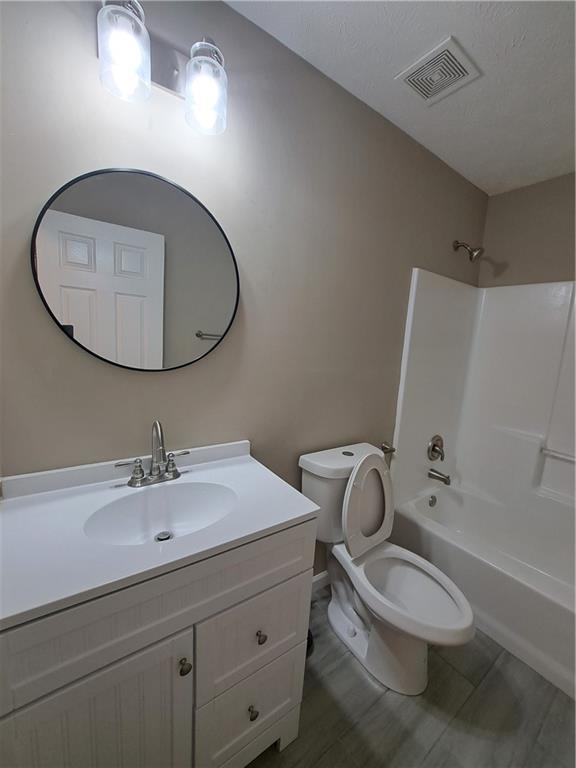 bathroom featuring visible vents, wood finished floors, vanity, toilet, and shower / bathtub combination