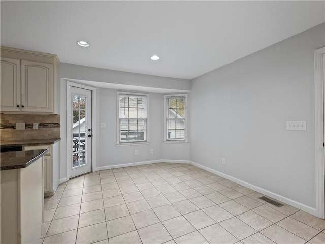 kitchen featuring backsplash, dark stone countertops, cream cabinets, and light tile patterned flooring