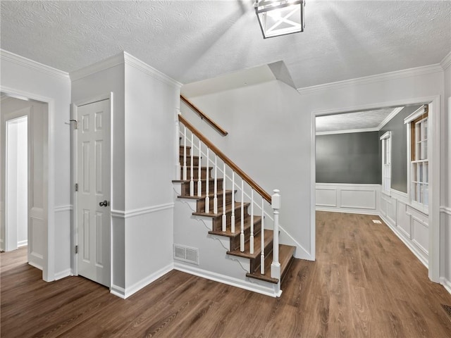 stairs with hardwood / wood-style flooring, ornamental molding, and a textured ceiling