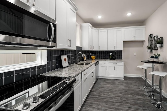 kitchen with light stone counters, white cabinets, sink, appliances with stainless steel finishes, and dark hardwood / wood-style flooring