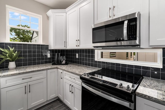 kitchen featuring appliances with stainless steel finishes, decorative backsplash, white cabinetry, and light stone countertops