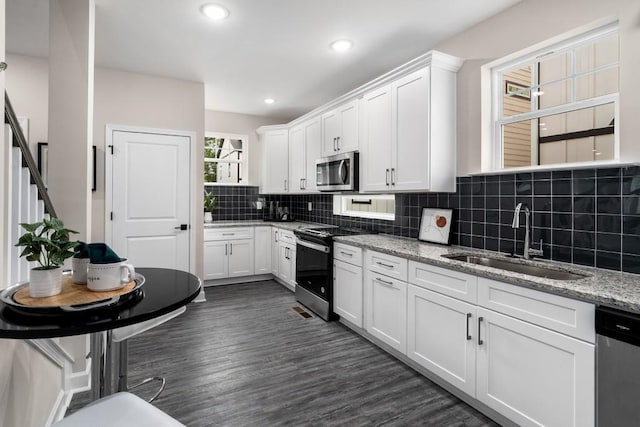 kitchen with appliances with stainless steel finishes, white cabinetry, light stone countertops, dark hardwood / wood-style floors, and sink