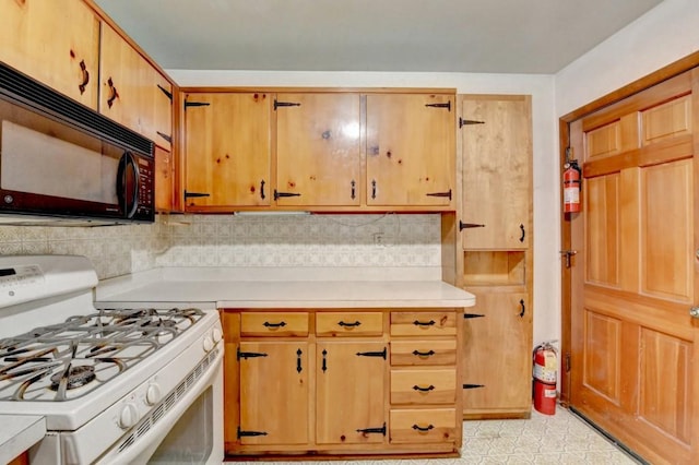 kitchen with white gas stove, tasteful backsplash, black microwave, light countertops, and light floors