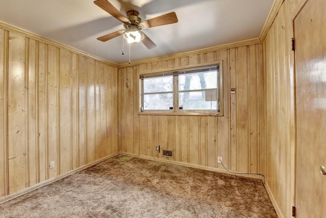 empty room featuring baseboards, wooden walls, a ceiling fan, and carpet