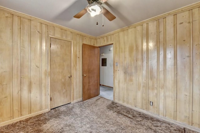 carpeted spare room featuring wooden walls and a ceiling fan