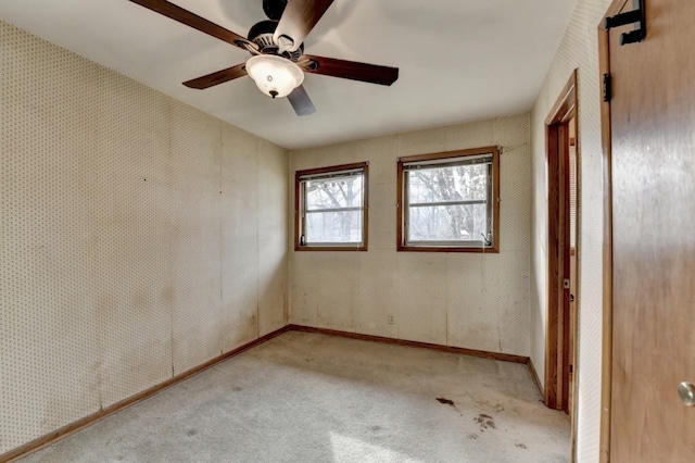 carpeted empty room featuring wallpapered walls, a ceiling fan, and baseboards