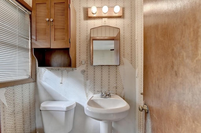 half bathroom with toilet, wallpapered walls, and a sink