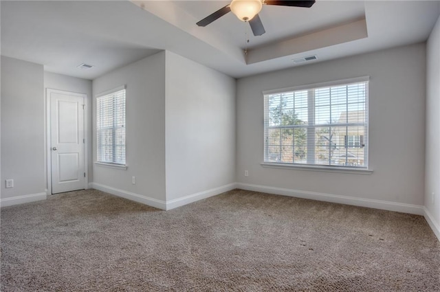 unfurnished room featuring a raised ceiling, ceiling fan, and carpet