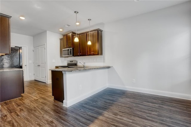 kitchen with light stone countertops, appliances with stainless steel finishes, kitchen peninsula, dark hardwood / wood-style floors, and hanging light fixtures