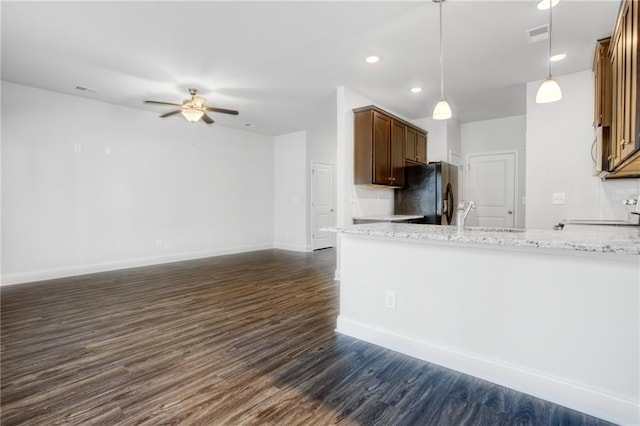 kitchen with hanging light fixtures, black fridge, light stone counters, dark hardwood / wood-style floors, and range