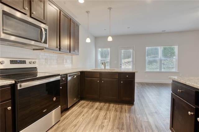 kitchen with appliances with stainless steel finishes, light wood-type flooring, backsplash, sink, and pendant lighting