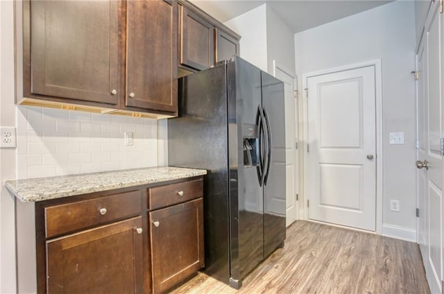 kitchen featuring light stone countertops, decorative backsplash, black refrigerator with ice dispenser, dark brown cabinetry, and light hardwood / wood-style floors