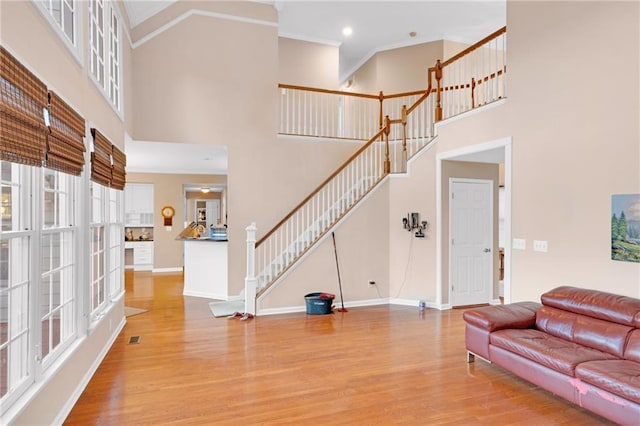 living room featuring ornamental molding, a towering ceiling, and light wood-type flooring